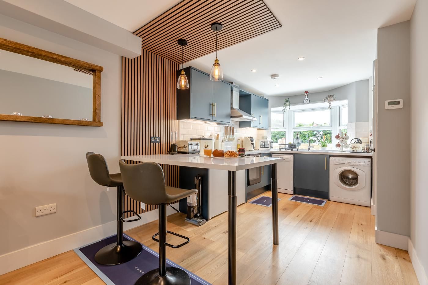 Een moderne keuken met een centraal eiland, barkrukken en een wasmachine.