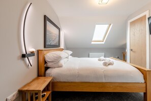 Ein Schlafzimmer mit Bett, Nachttisch, Wandregal, gerahmtem Bild, Oberlicht und Tür.