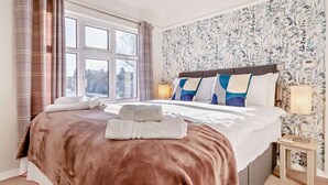 Une chambre d’hôtel avec un grand lit, une table de chevet, une commode et une fenêtre avec des rideaux.