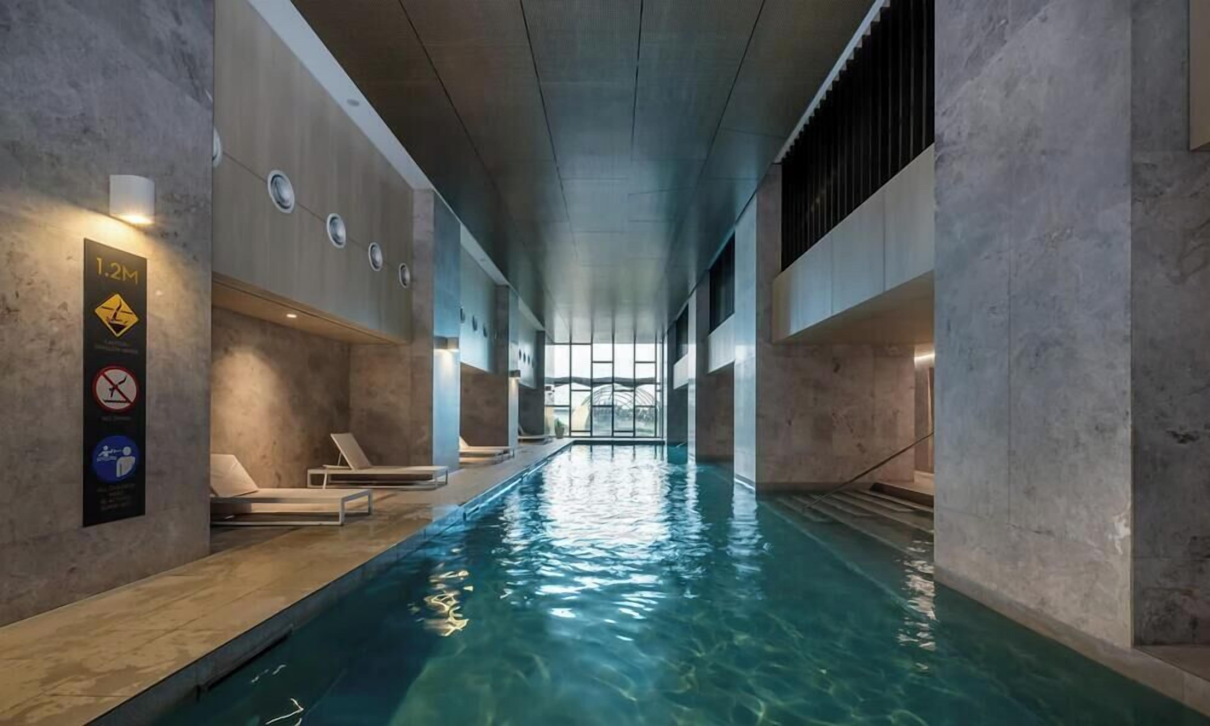 An indoor swimming pool with clear water, lounge chairs, and a sign indicating a 1.2M depth.