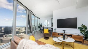 Een moderne woonkamer met een grote televisie, een bank, een eethoek en uitzicht op de stad.