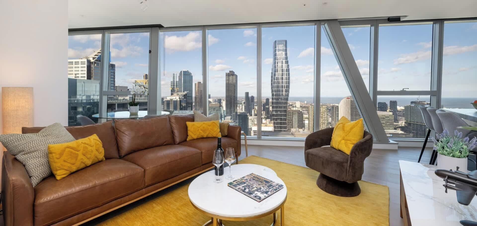 A modern living room with a city view, a brown leather sofa, a round coffee table, and a unique chair.
