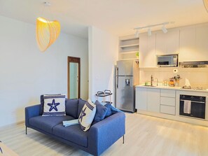 A modern apartment with a grey sofa, a kitchen with white cabinets, a stainless steel refrigerator, and a hanging light fixture. - The Nautique - Loft front beach (Arraiján)