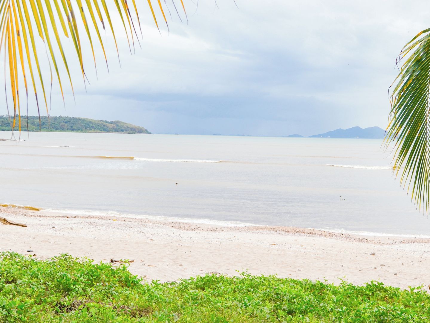 A beach with calm waters, a sandy shore, and distant landforms.