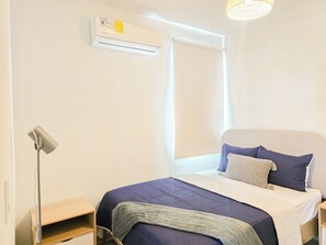 Une chambre à coucher avec un lit, une lampe de chevet, une fenêtre et un appareil de climatisation.