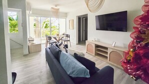 Ein modernes Wohnzimmer mit einer Couch, einem Fernseher und einem Essbereich mit Stühlen und einem Tisch.