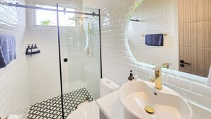 Ein modernes Badezimmer mit einer Glaskabine zur Dusche, einem weißen Waschbecken und einem großen Spiegel.