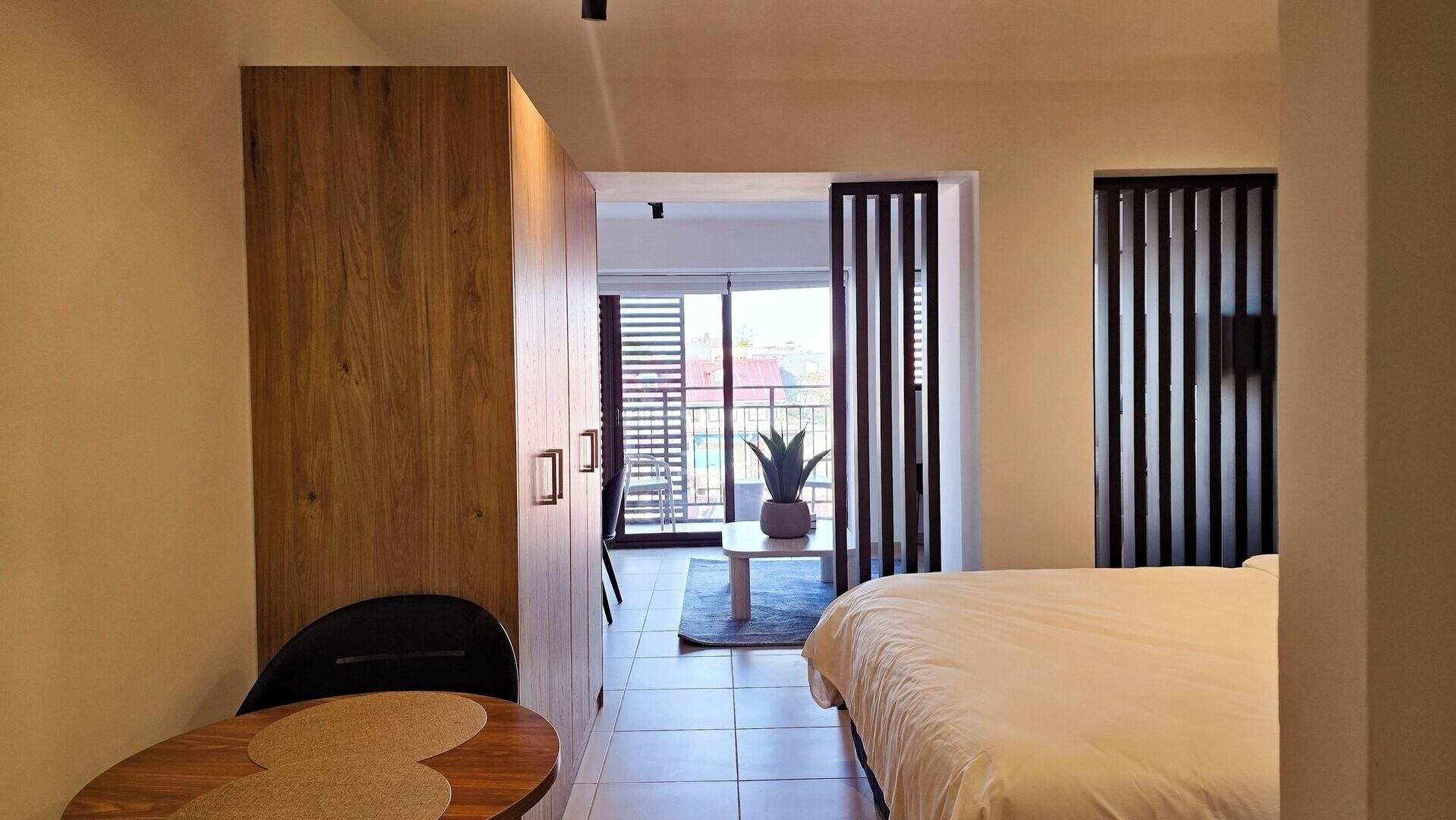 A bedroom with a bed, a small table, a chair, and a potted plant.