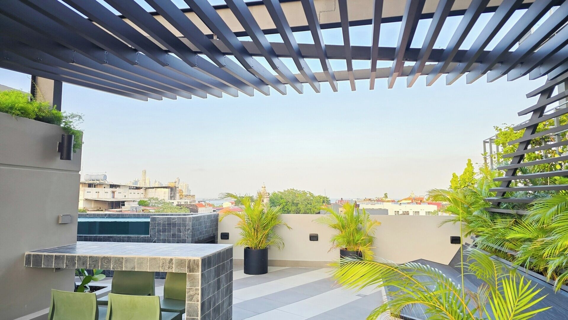 A rooftop terrace with a pergola, outdoor seating, potted plants, and a city view.