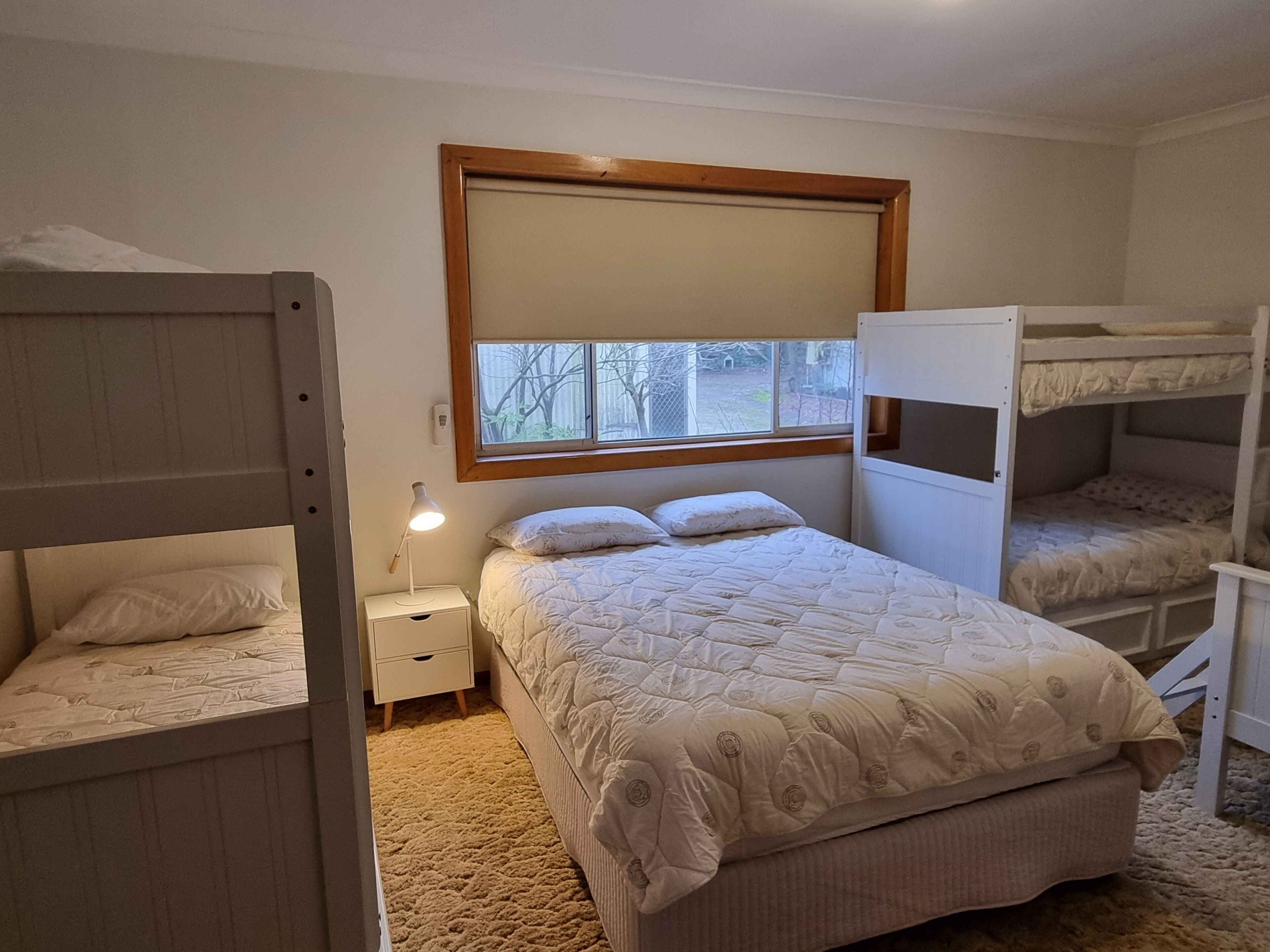 A bunk bed room with a window, a bedside lamp, and a carpeted floor.