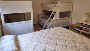 A room with bunk beds, a bed with a patterned duvet, and a small shelf with folded clothes.