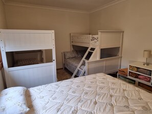 A room with bunk beds, a bed with a patterned duvet, and a small shelf with folded clothes.
