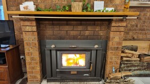 A brick fireplace with a wood-burning stove, a television on a stand to the left, and a shelf above the fireplace with decorative items.