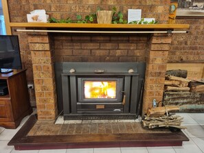A brick fireplace with a wood-burning stove, a television on a stand to the left, and a shelf above the fireplace with decorative items.