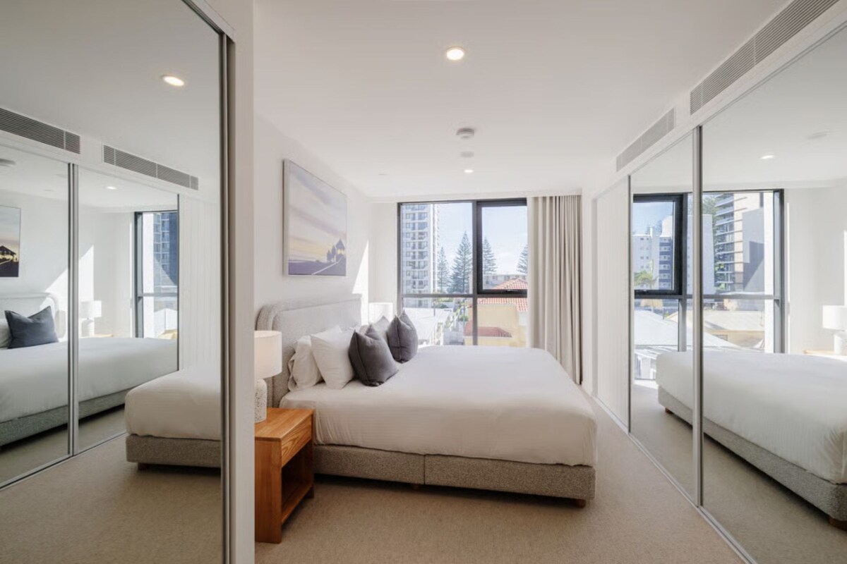 Ein modernes Hotelzimmer mit einem großen Bett, einem Nachttisch, einem Spiegel und Blick auf die Stadt.