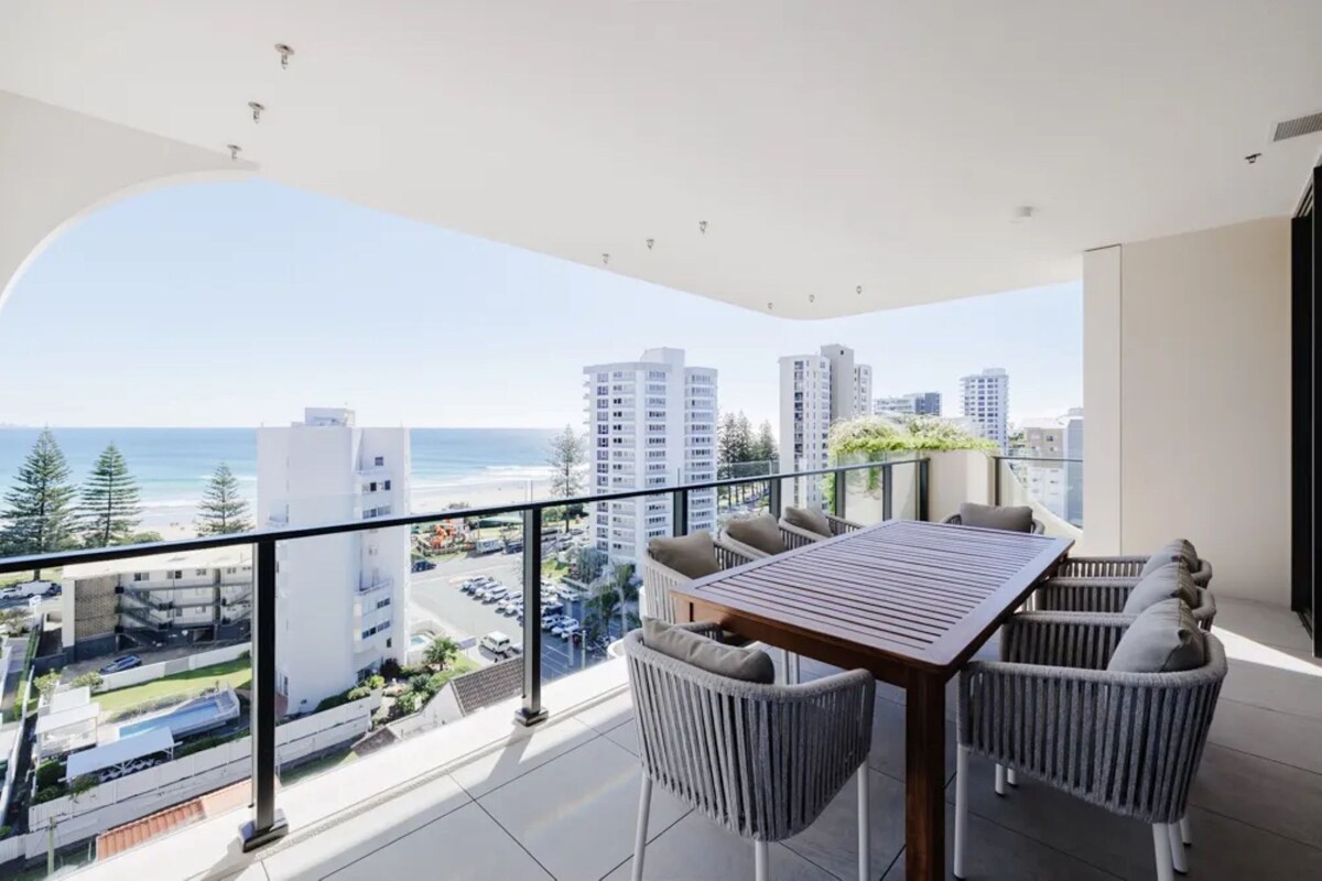 Ein Balkon mit Tisch und Stühlen, mit Blick auf Strand und Stadtlandschaft.