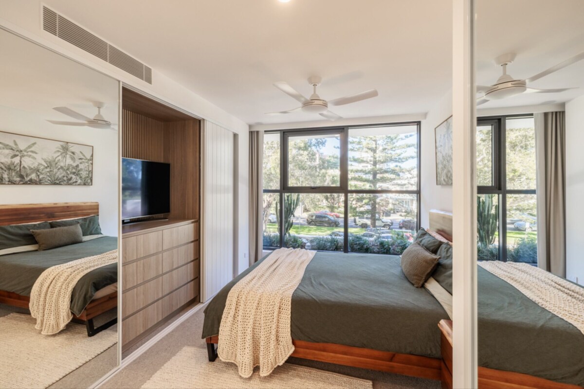 Ein Schlafzimmer mit großem Fenster, Deckenventilator und Flachbildfernseher.