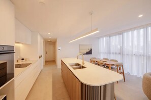 Eine moderne Küche mit Kochinsel, ein Essbereich mit Tisch und Stühlen sowie ein großes Fenster mit transparenten Vorhängen.