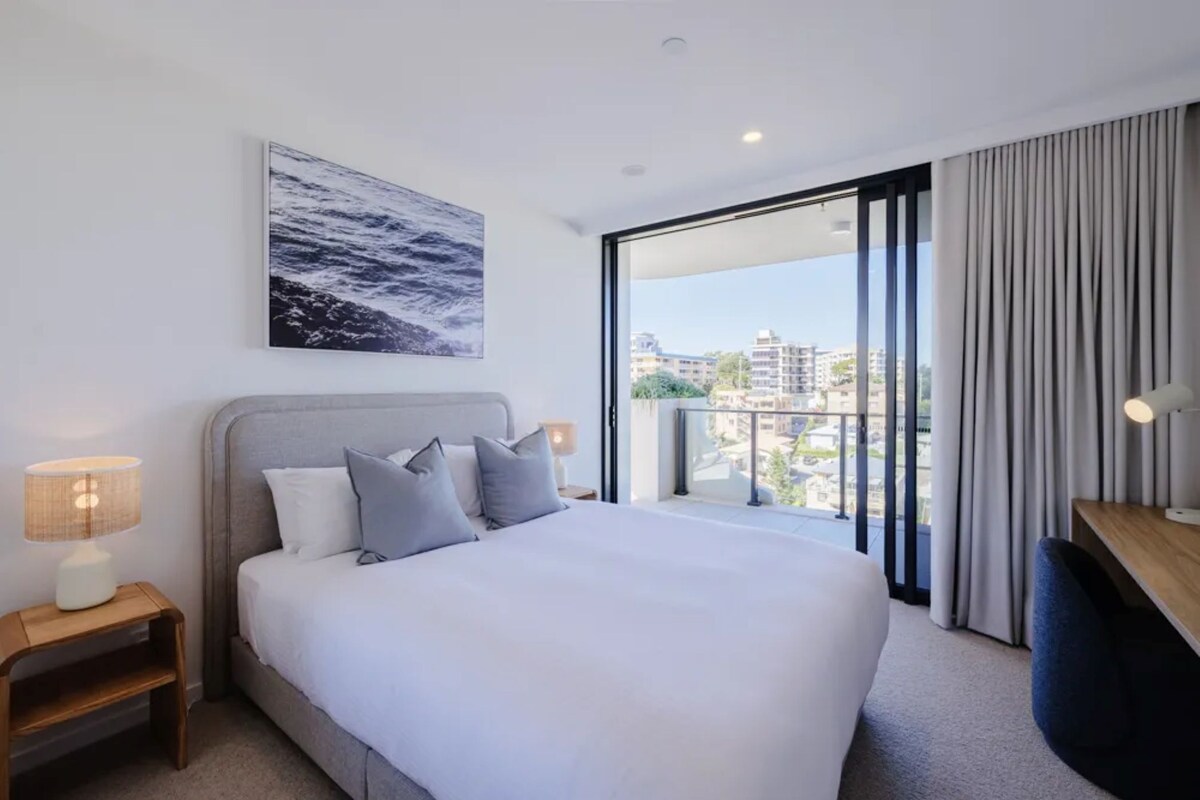 Ein modernes Hotelzimmer mit einem großen Bett, einem Nachttisch, einer Lampe und Blick auf die Stadt vom Balkon aus.