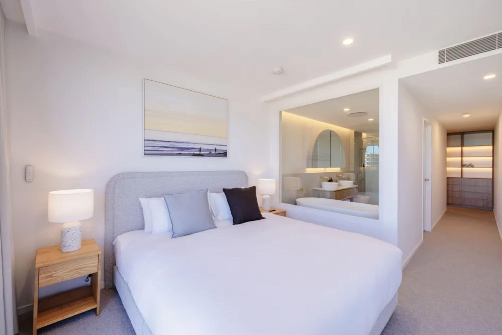 Quarto de hotel com uma cama grande, mesas de cabeceira, um espelho e vista para o banheiro.