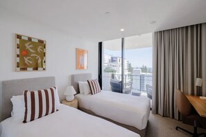 Ein Hotelzimmer mit zwei Betten, einem Schreibtisch, einem Stuhl, einem fenster mit Vorhängen und Bildern an der Wand.