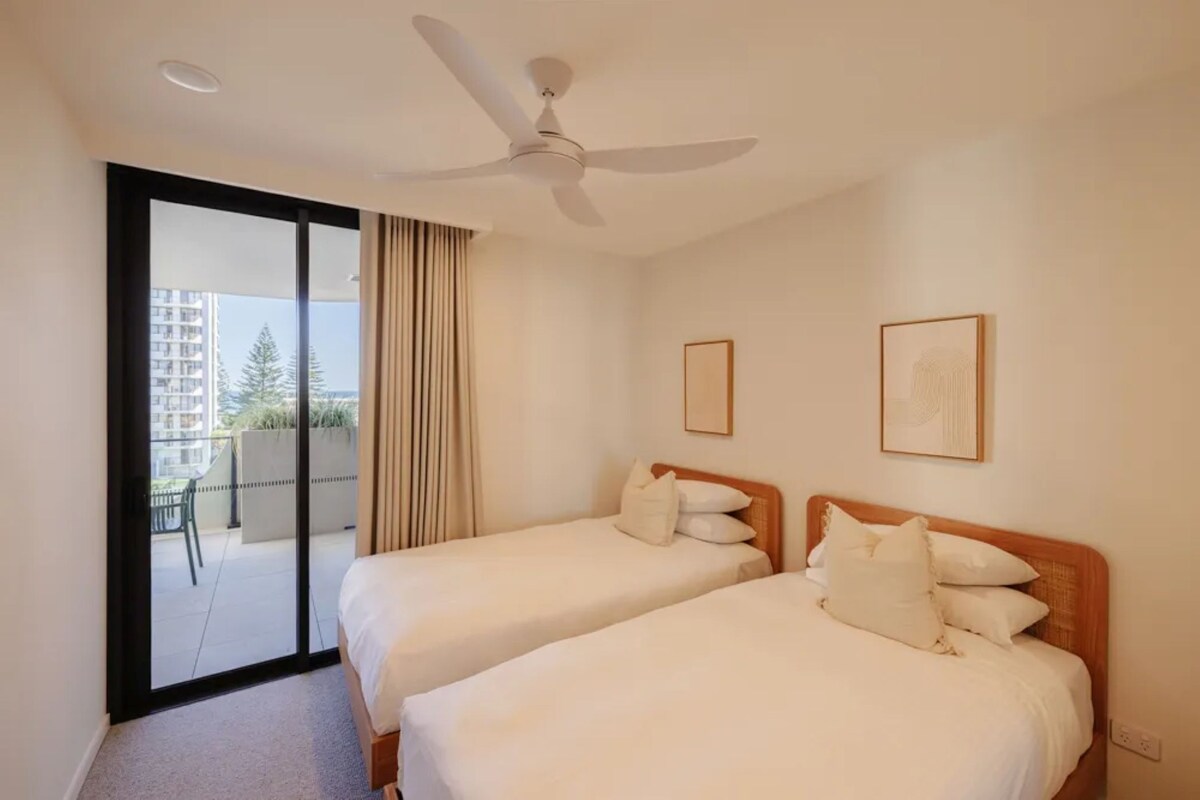 Ein Hotelzimmer mit zwei Betten, einem Deckenventilator, einer Schiebetür zu einem Balkon und zwei gerahmten Bildern an der Wand.
