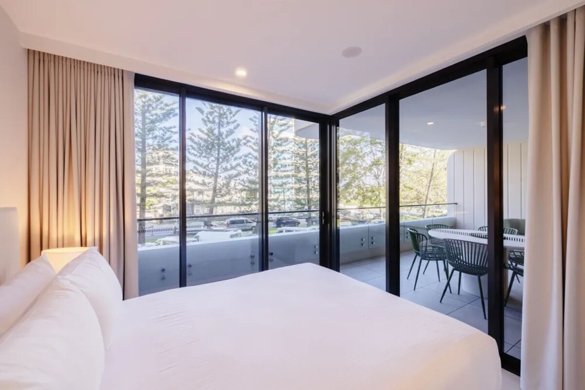 Ein Hotelzimmer mit einem großen Bett, einem Schreibtisch und einem Balkon mit Blick auf Bäume und parkende Autos.