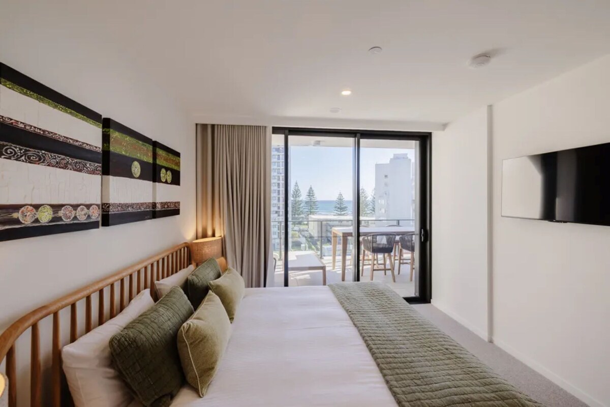 Ein Hotelzimmer mit Bett, Fernseher, einem Balkon mit Tisch und Stühlen sowie Bildern an der Wand.