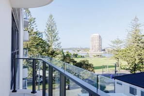 Ein modernes Gebäude mit einem Glasbalkon mit Blick auf eine Stadtlandschaft, darunter ein hoher Wolkenkratzer und ein Park.