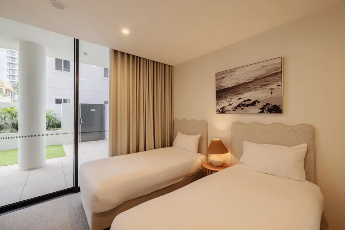 Ein Hotelzimmer mit zwei Betten, einem großen Fenster, einem Gemälde und Blick ins Freie.