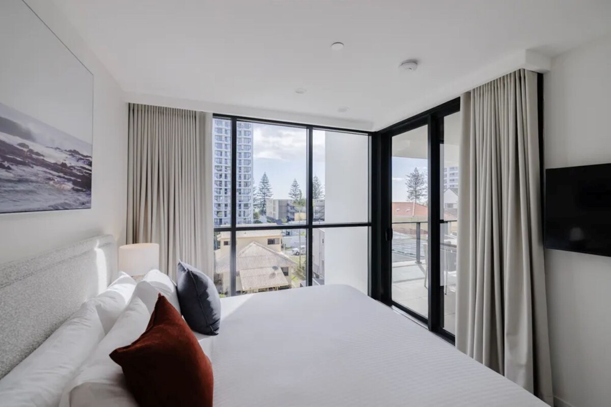 Ein Hotelzimmer mit einem großen Bett, einem Fenster mit Vorhängen, einem Flachbildfernseher und einem Gemälde an der Wand.