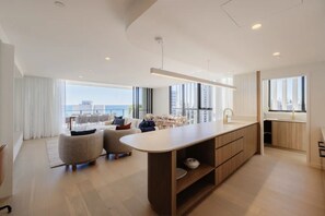A modern kitchen with a central island, dining area with chairs, and large windows offering a view of the city. - Esprit Holidays Rainbow Bay (Coolangatta)