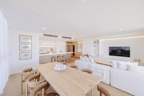 Ein modernes Wohnzimmer mit einem Holzesstisch, weißen Sofas und einem an der Wand befestigten Flachbildfernseher.
