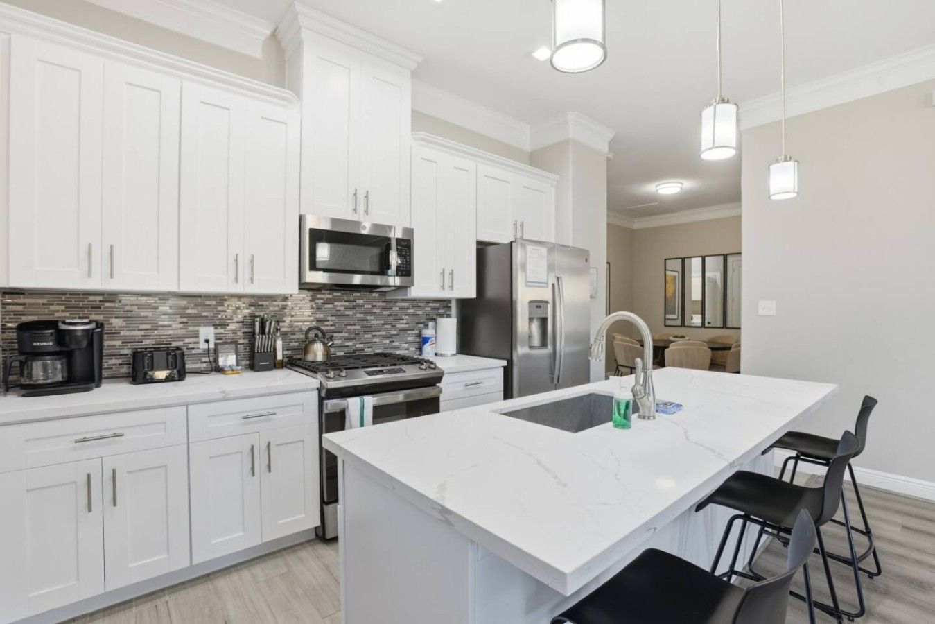 A modern kitchen with white cabinetry, stainless steel appliances, and a marble island.
