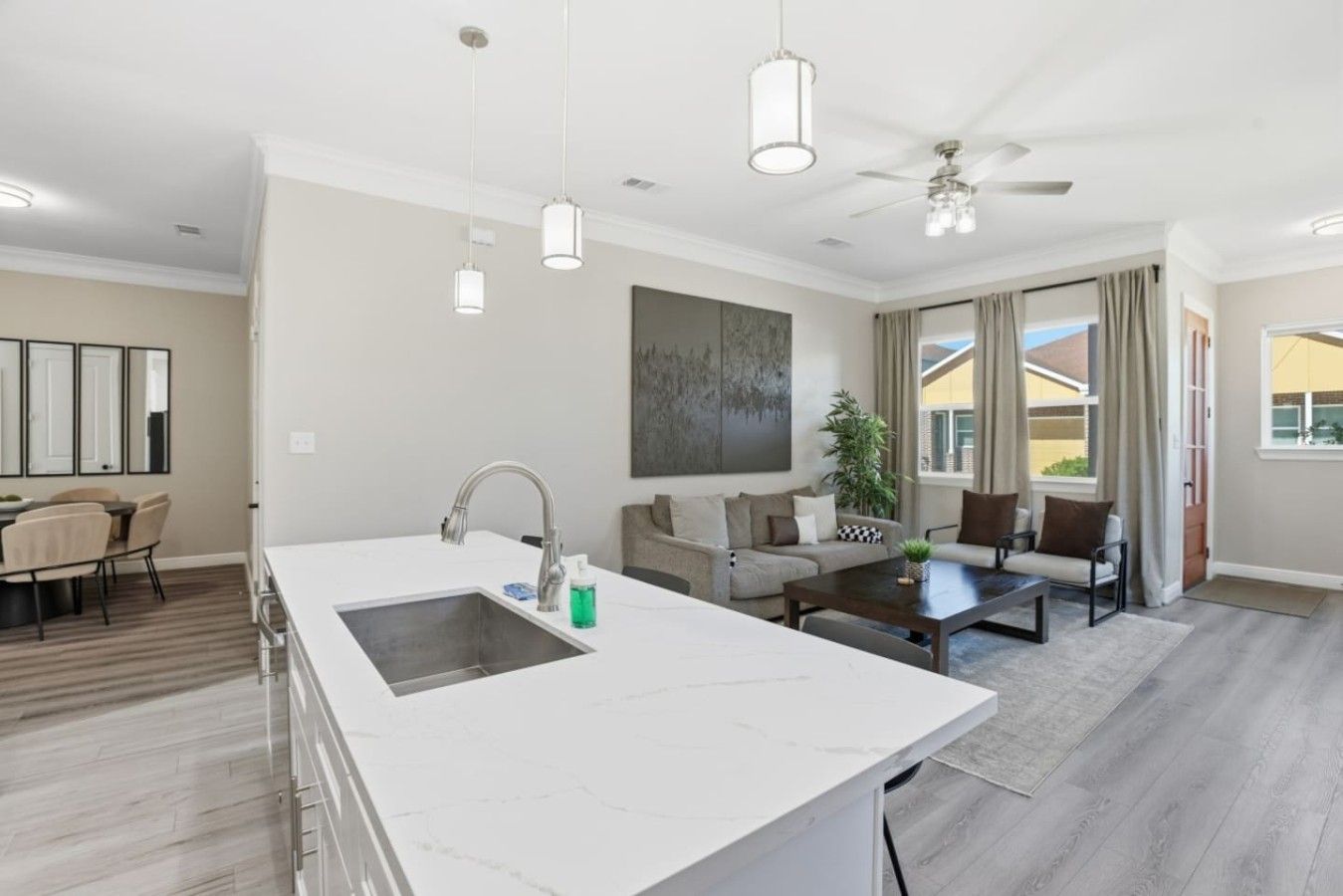 A modern kitchen with a large island, a dining area with a table and chairs, a sofa, and a ceiling fan.