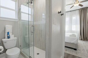 Ein Hotelbad mit einer Duschkabine, einer Toilette und einem Bett mit weißer Bettdecke.