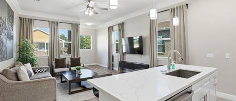 A modern kitchen with a large island, a dining area with a sofa and table, and a ceiling fan.