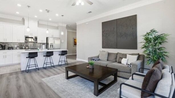 Una cocina moderna con armarios blancos, una zona de bar y un espacio comedor con una mesa baja de color oscuro.