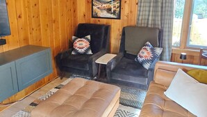 Een houten interieur met een bank, twee fauteuils, een bijzettafeltje en een televisie.