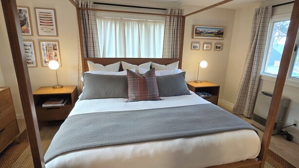 Een bed met hemelbed, een hoofdbord, twee nachtkastjes, een raam met gordijnen en een wanddecoratie.