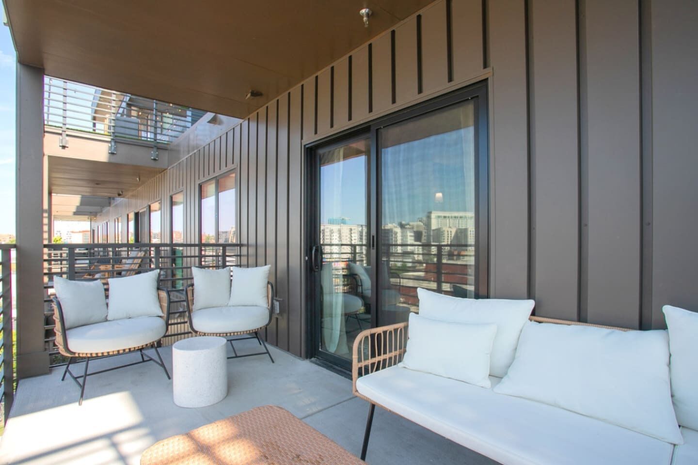 A balcony with a sofa, two chairs, a small table, and a glass door leading to a city view.