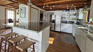 Una cocina con vigas de madera, una isla central con taburetes, armarios blancos y un refrigerador.