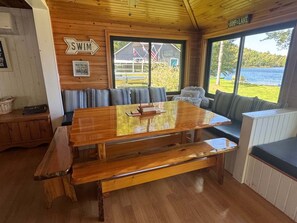 A wooden cabin with a large dining table, benches, and a view of a lake.