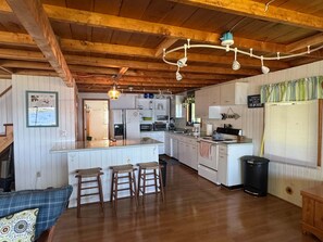 A cozy cabin interior with a wooden ceiling, a kitchen area, a dining space, and a living area with a sofa and stools.