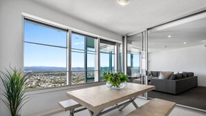 A modern living room with a large window, a dining table, and a sofa. - Elevé at Q1 - Spectacular Beach + Hinterland views (Surfers Paradise)