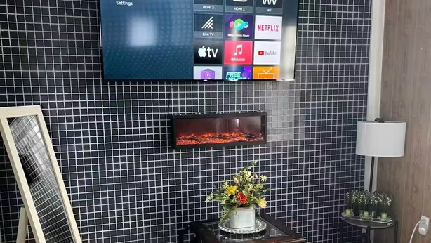 Ett modernt rum med en stor platt-TV som är monterad på en kaklad vägg och som visar gränssnittet för en streamingtjänst.