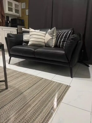 Eine schwarze Ledersofa mit gestreiften Kissen, ein gewebter Teppich und ein Küchenbereich im Hintergrund.