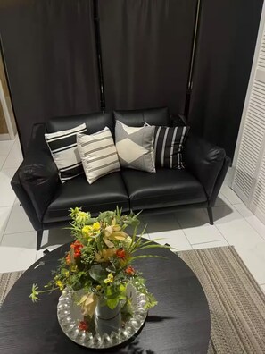 Un canapé en cuir noir agrémenté de coussins à rayures et unis, une table ronde noire ornée d’un centre de table floral et un tapis à motifs.