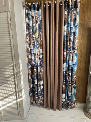 Ein Zimmer mit einem Fenster, das mit einem Vorhang mit blau-braunem, abstrakten Muster verziert ist.