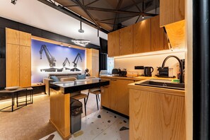 A modern kitchen with wooden cabinets, a black countertop, and a dining area with a sofa and chairs. - 100 Steps to Old Town Beza Apartment (Gdańsk)